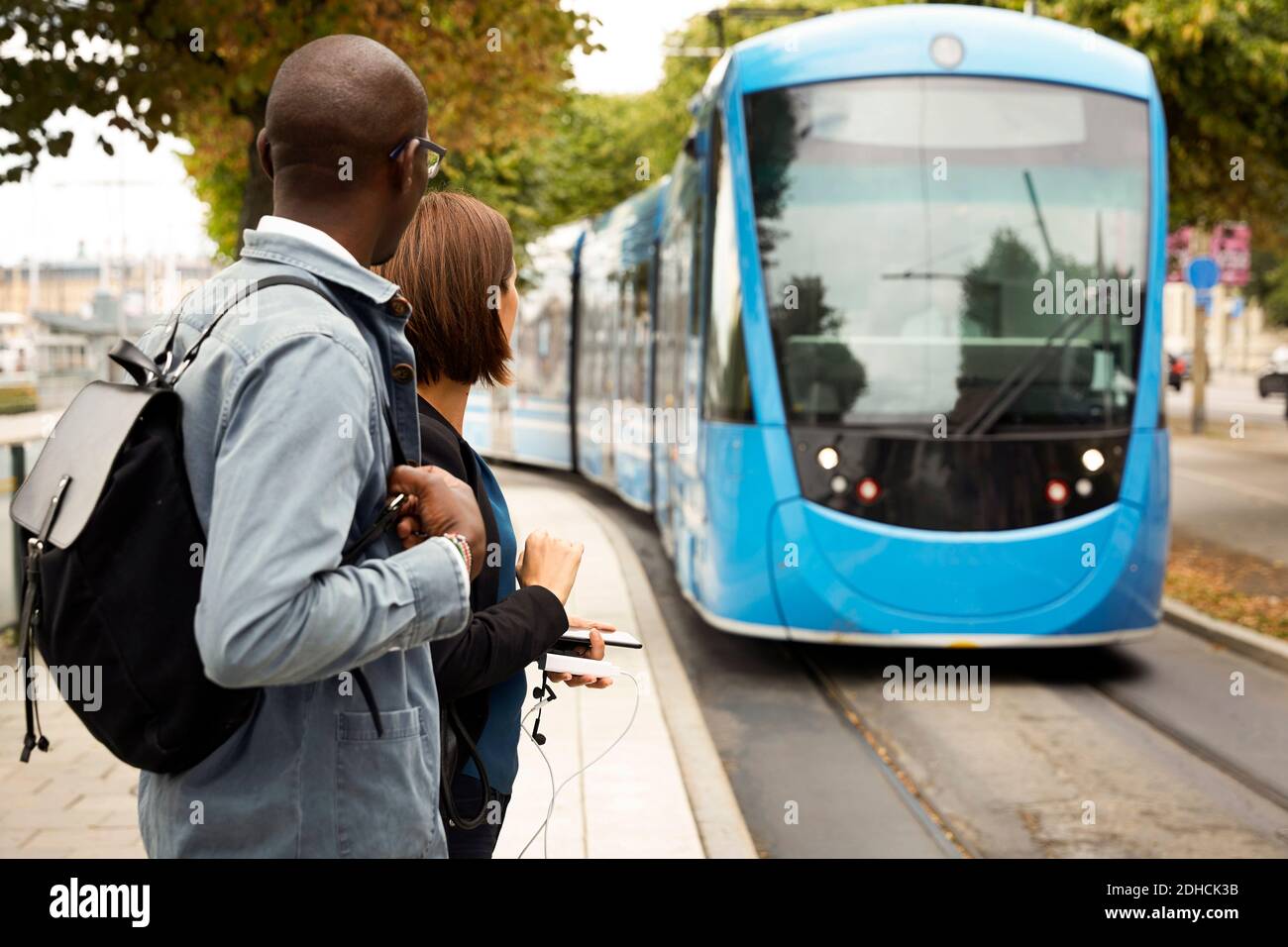 Pendolari in attesa sul marciapiede mentre si guarda il tram blu in città Foto Stock