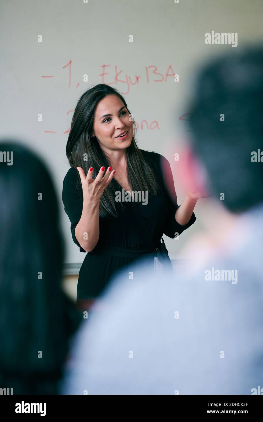 Donna mid adulta gesturing mentre insegna gli studenti nella scuola di lingua Foto Stock