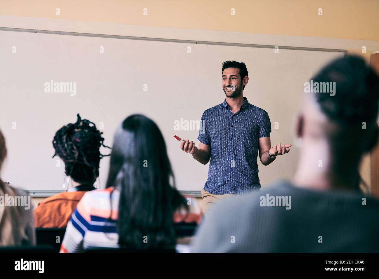 Giovane insegnante di sesso maschile sorridente mentre insegna agli studenti nella scuola di lingua Foto Stock