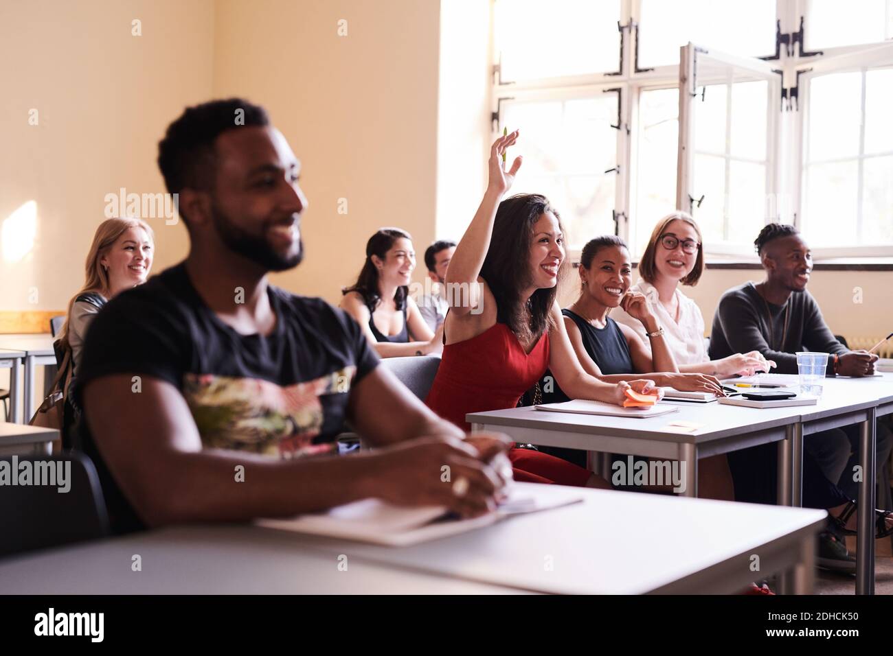 Donna felice alzando il braccio per rispondere in classe di lingua Foto Stock