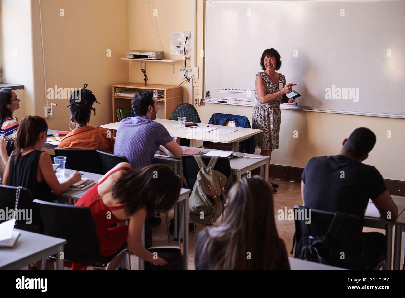 Insegnante femminile sorridente mentre insegna agli studenti in classe di lingua Foto Stock