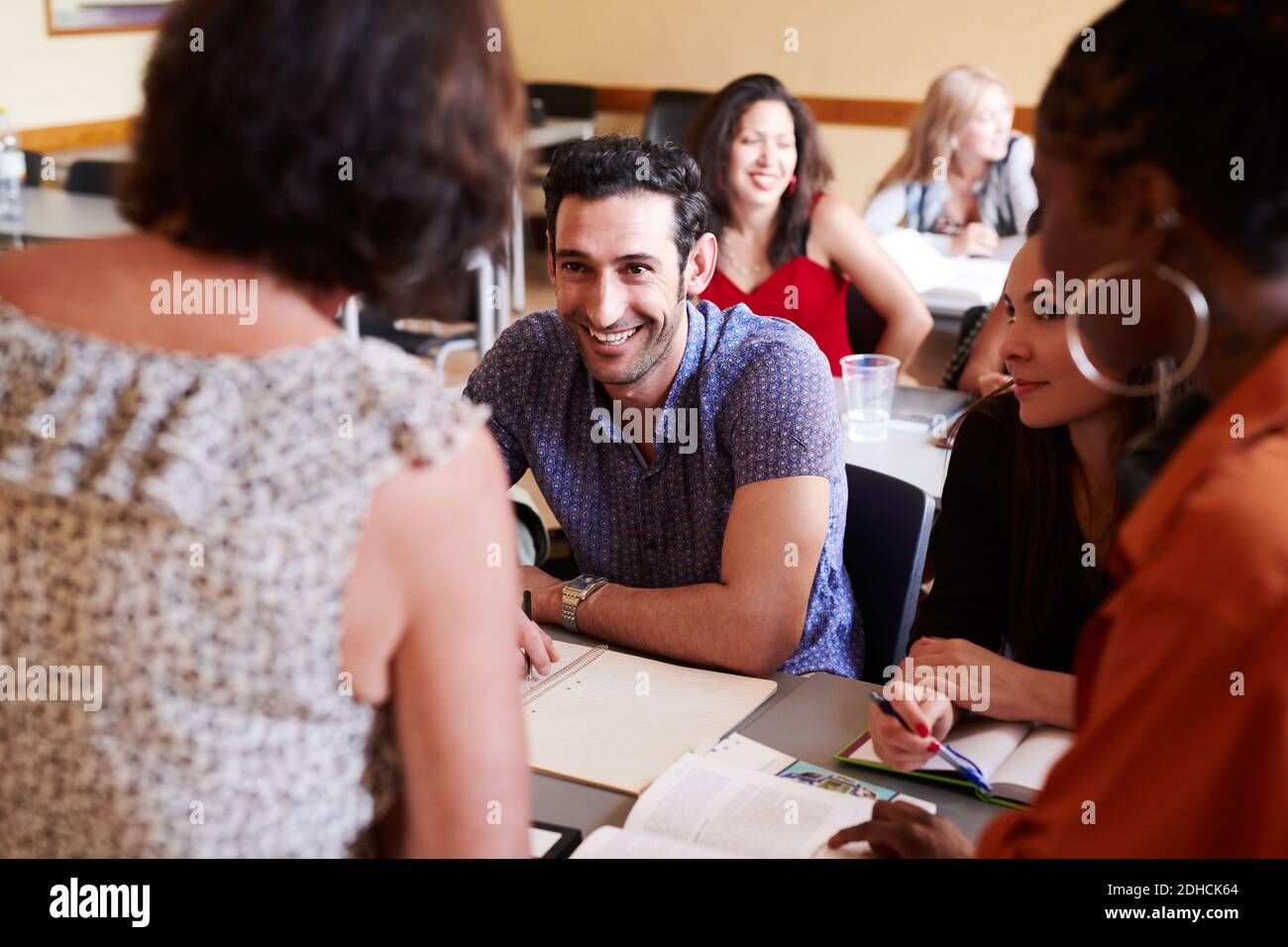 Felice studente di sesso maschile che guarda l'insegnante mentre si siede con gli amici nella scuola di lingua Foto Stock