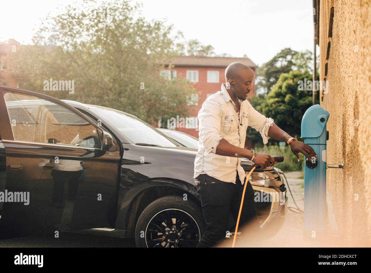 Uomo che collega il cavo elettrico per caricare l'auto elettrica a. stazione Foto Stock
