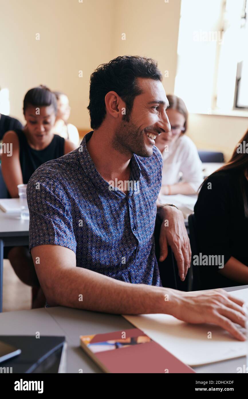 Giovane uomo sorridente mentre si guarda via nella scuola di lingua Foto Stock