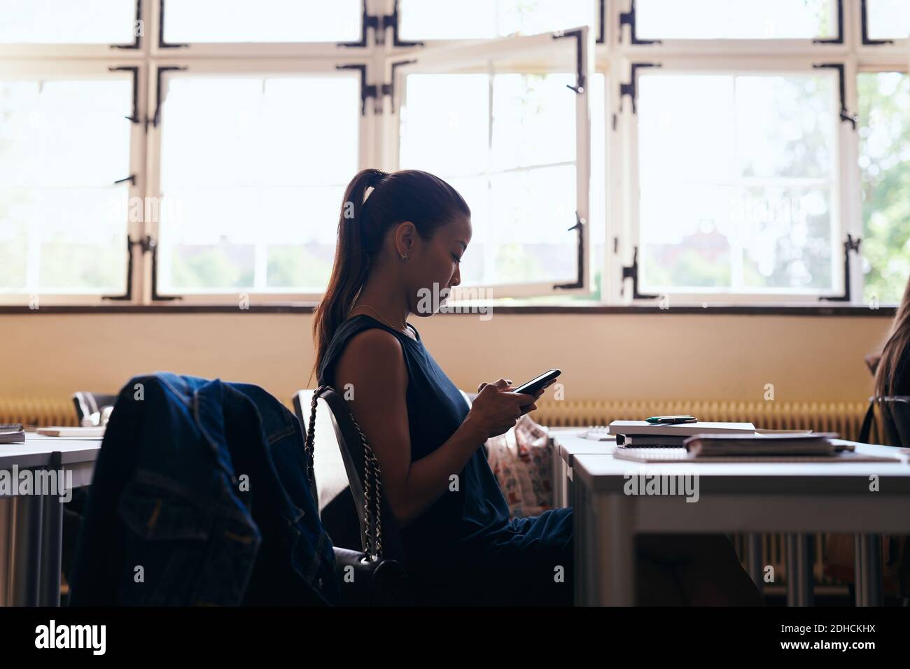 Vista laterale della donna che utilizza il telefono cellulare mentre è seduto scuola di lingua Foto Stock