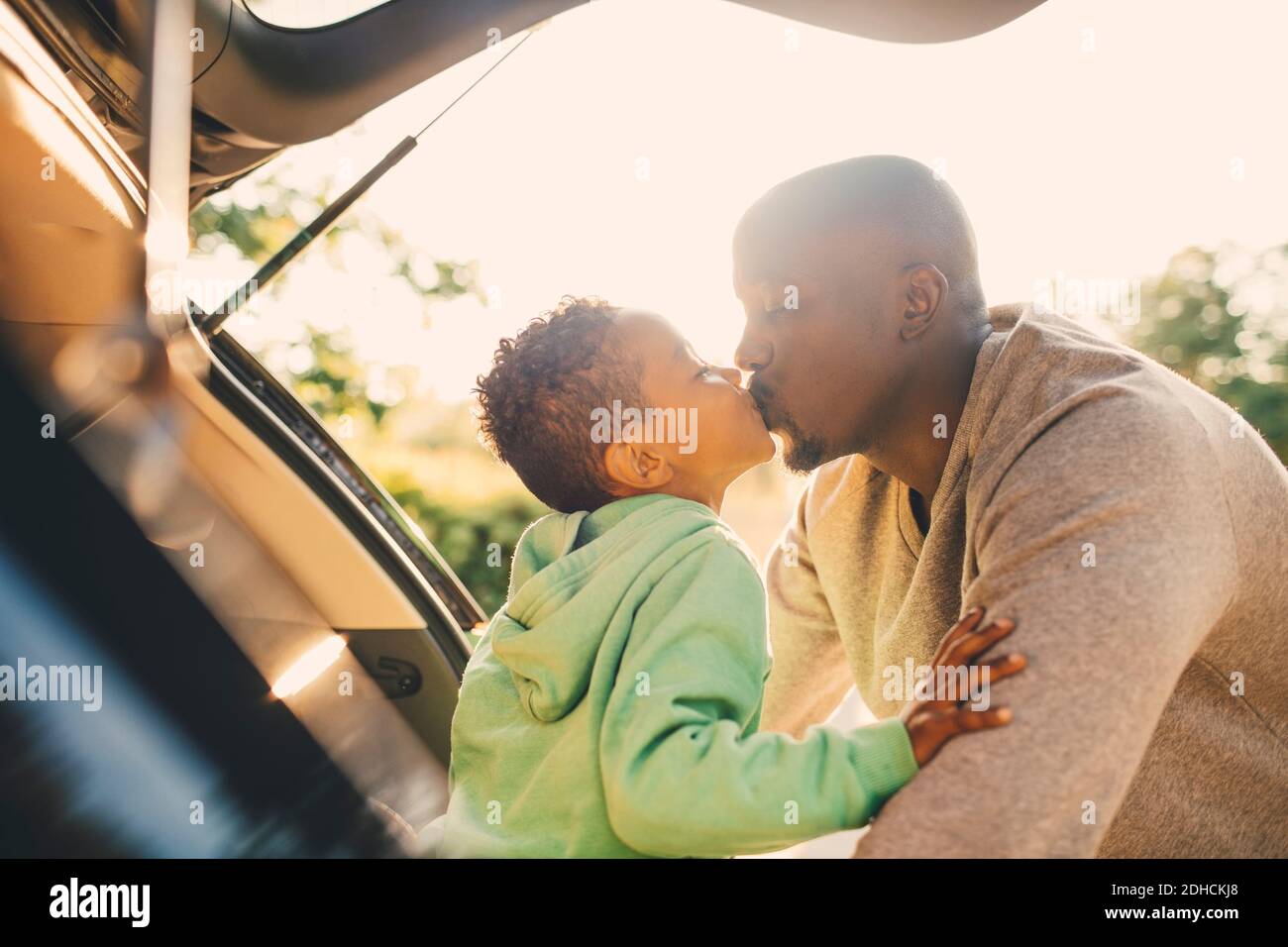 Padre baciando il figlio seduto nel bagagliaio dell'auto Foto Stock