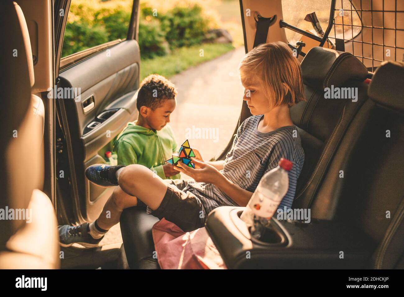 Ragazza che gioca a puzzle cubo mentre si siede in auto da fratello al parco Foto Stock