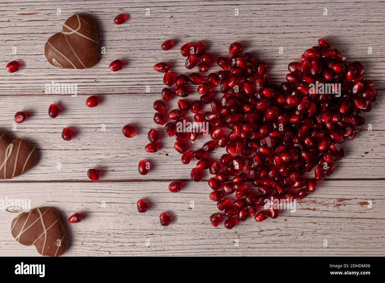 Semi di melograno disposti a forma di cuore mobile con uno striscio di semi che si disintegra come coda. Biscotti a forma di cuore sul lato. Un dolce e delizioso c Foto Stock