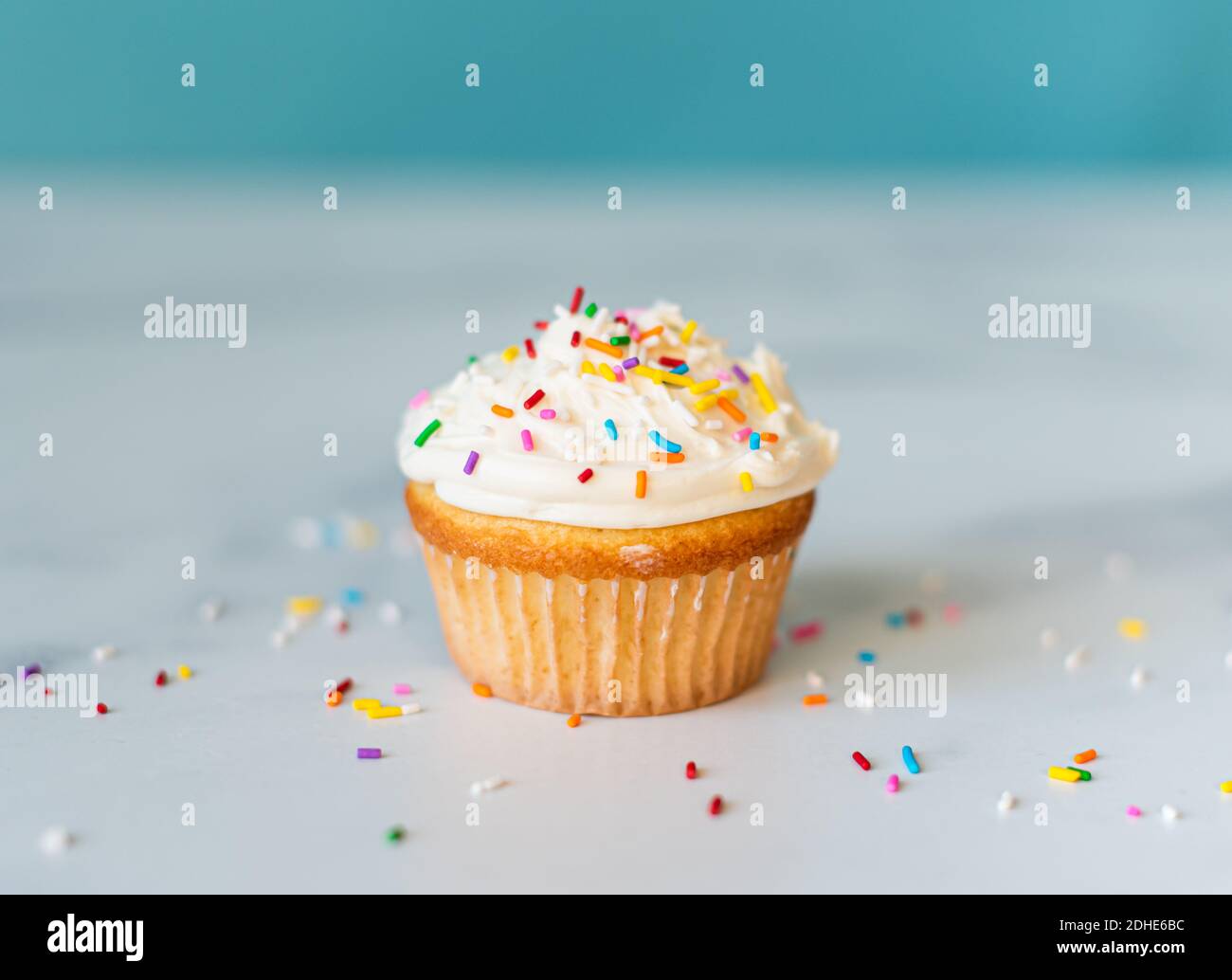 Cupcake ghiacciato alla vaniglia con spruzzini su una superficie bianca. Foto Stock