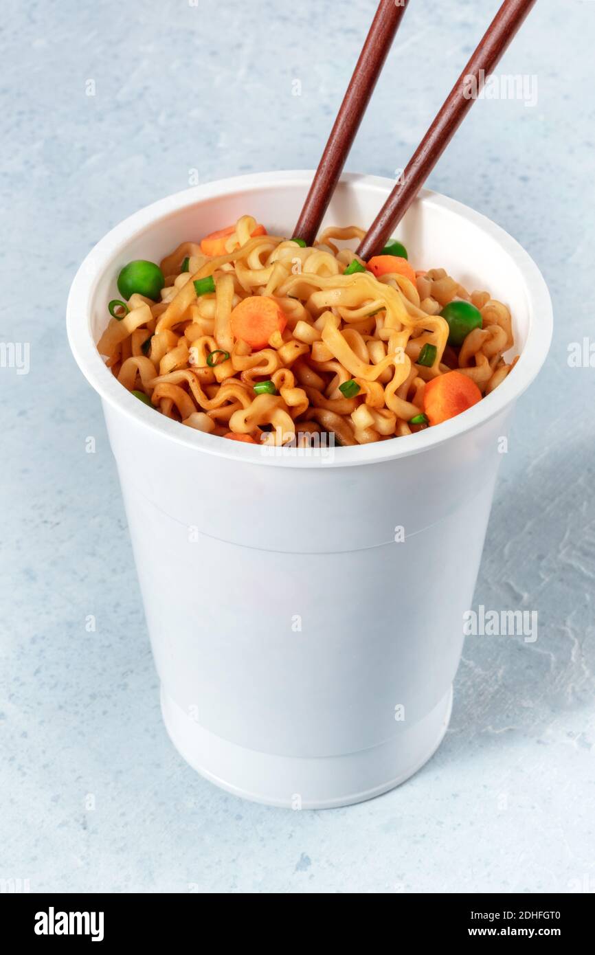 Tagliatelle istantanee con bastoncini in una tazza di plastica Foto Stock
