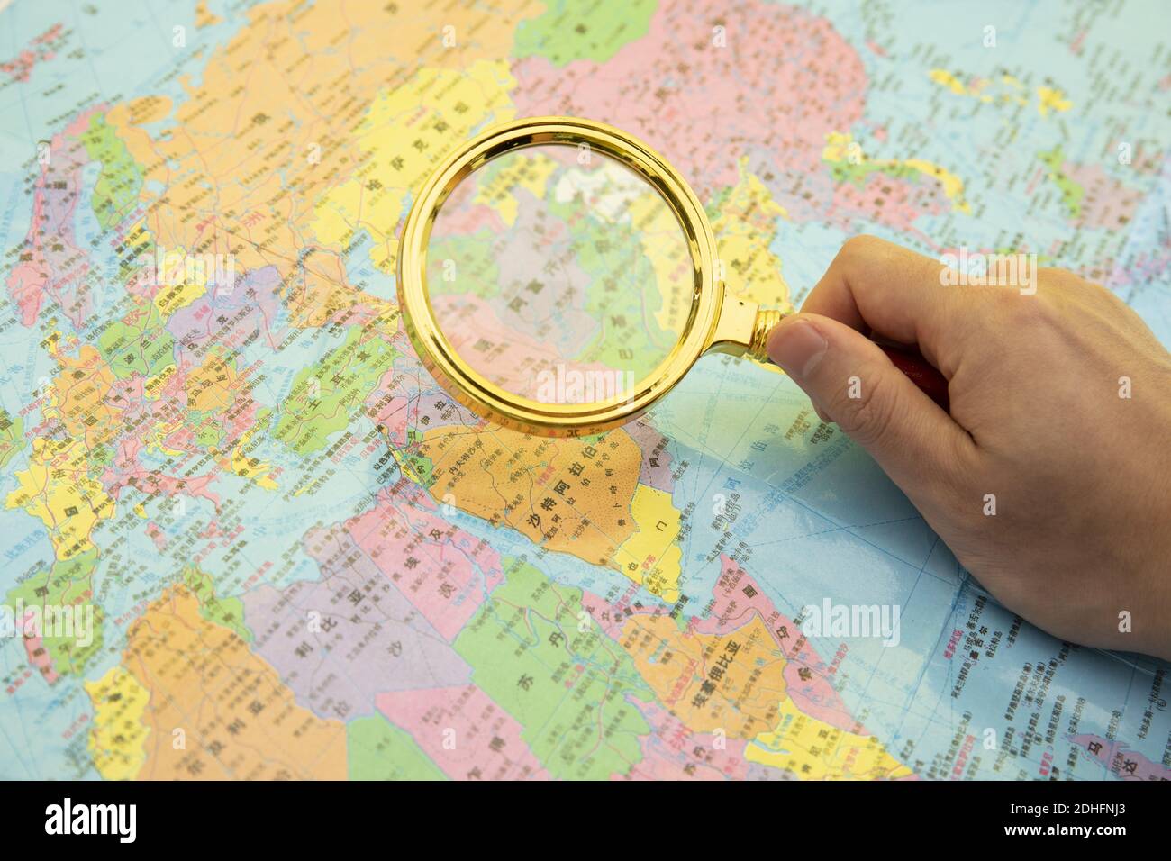 Un primo piano di una mano che tiene una lente d'ingrandimento sopra mappa del mondo background-concetto di viaggio e avventura Foto Stock