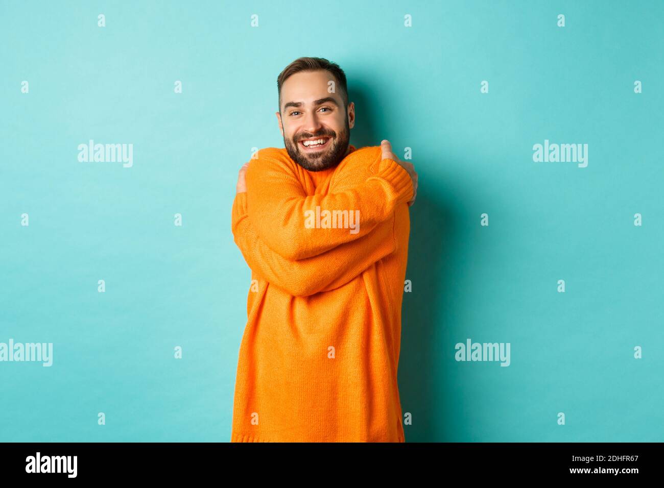 L'uomo felice si sente comodo, indossa un maglione caldo e si agguantano, sorridente soddisfatto, in piedi su sfondo azzurro chiaro Foto Stock