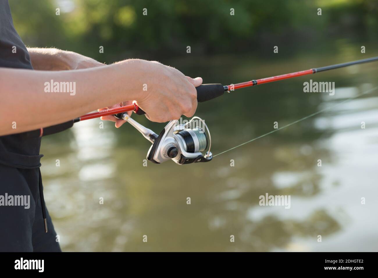 Le mani del pescatore tengono una pesca che gira sopra l'acqua mentre pesca. Foto Stock