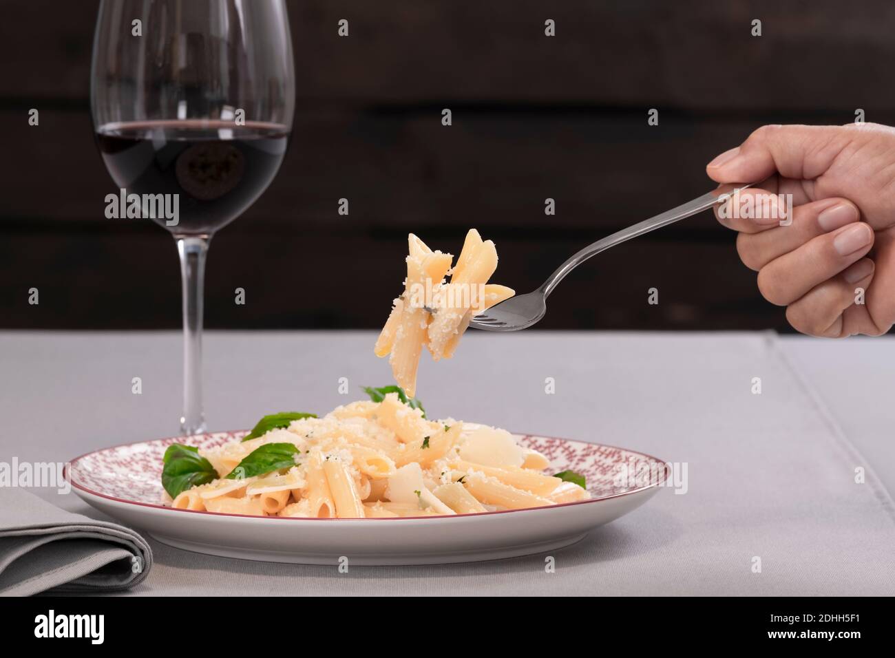 Fuoco selettivo di pasta appena cotta con formaggio su una forchetta tenuta da una mano su un piatto con un bicchiere di vino fuori fuoco. Concetto di stile di vita. Foto Stock