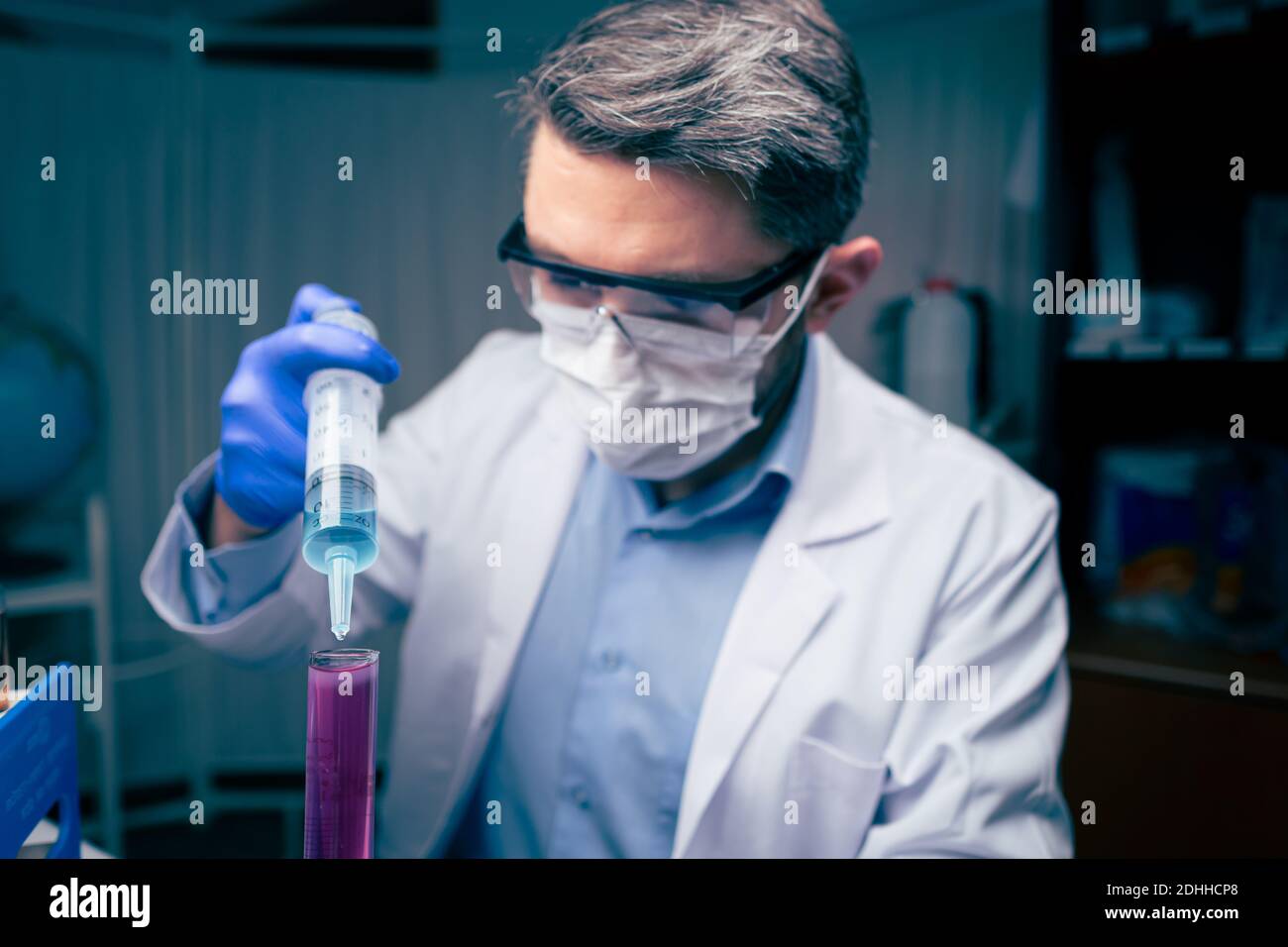 Giovane scienziato guardare una provetta in laboratorio. L'uomo indossa occhiali di protezione Foto Stock