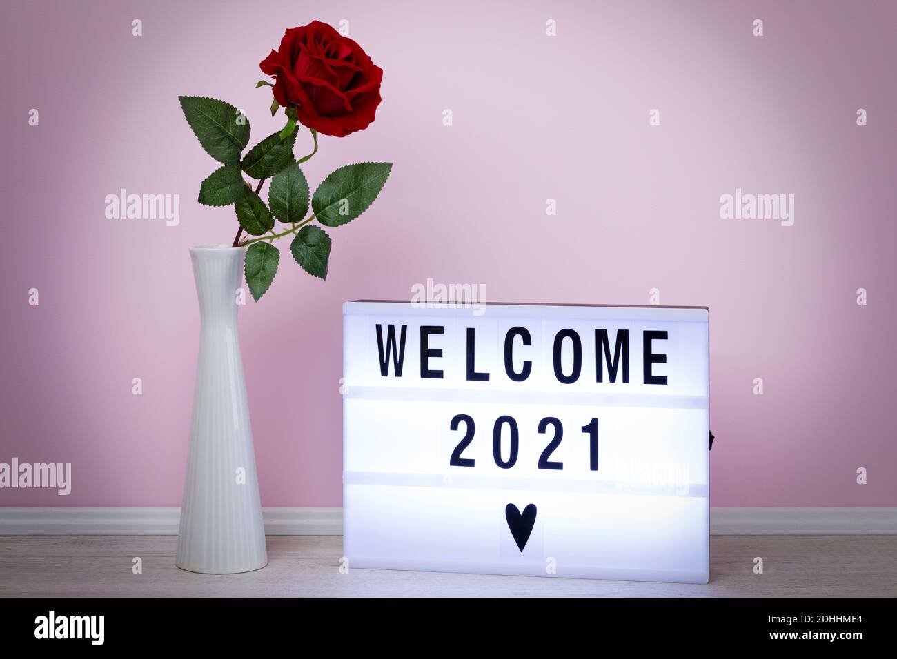 Welcome 2021, messaggio scritto su lightbox, con falsa rosa in vaso di fronte alla parete rosa Foto Stock