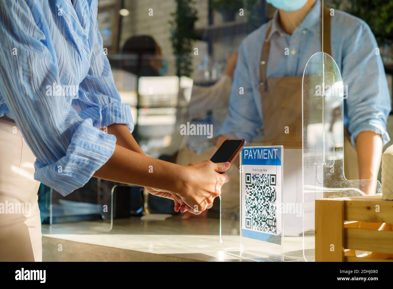 Donna asiatica che utilizza il pagamento tramite scansione mobile QR o NFC su smartphone pagare per la sua bevanda di caffè in caffè Negozio e plexi schermo e Barista indossato Foto Stock
