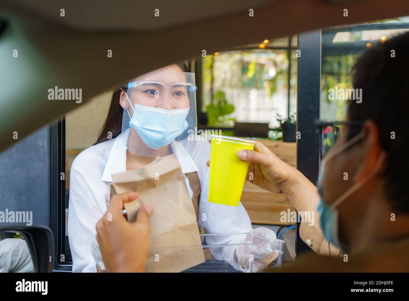 Uomo asiatico in maschera protettiva prendendo sacchetto di cibo e caffè con cameriera donna che indossa maschera facciale e visiera a. guida attraverso durante il coronavirus outbera Foto Stock
