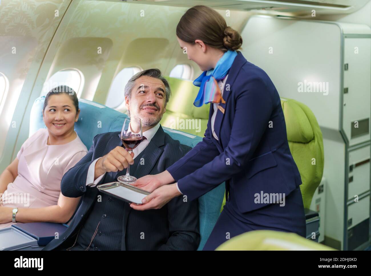 Il personale di Air Hostess in aereo serve vino rosso a un uomo d'affari in Business Class alla cabina passeggeri in aereo. Foto Stock