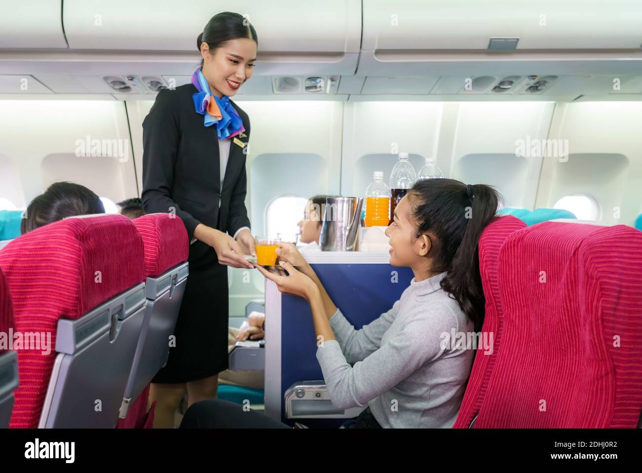 Il personale di una compagnia aerea in aereo serve succo d'arancia alla donna in classe economica in cabina passeggeri in aereo. Foto Stock