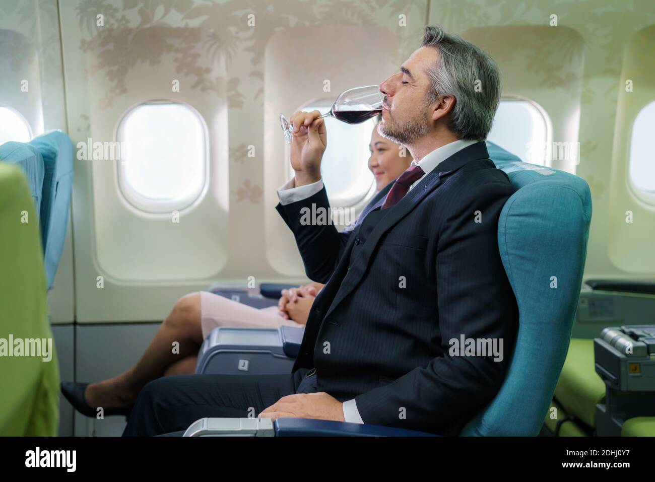 Durante il volo un uomo d'affari passager che tiene un bicchiere di spumante e che beve in Business Class alla cabina dell'aeroplano. Foto Stock