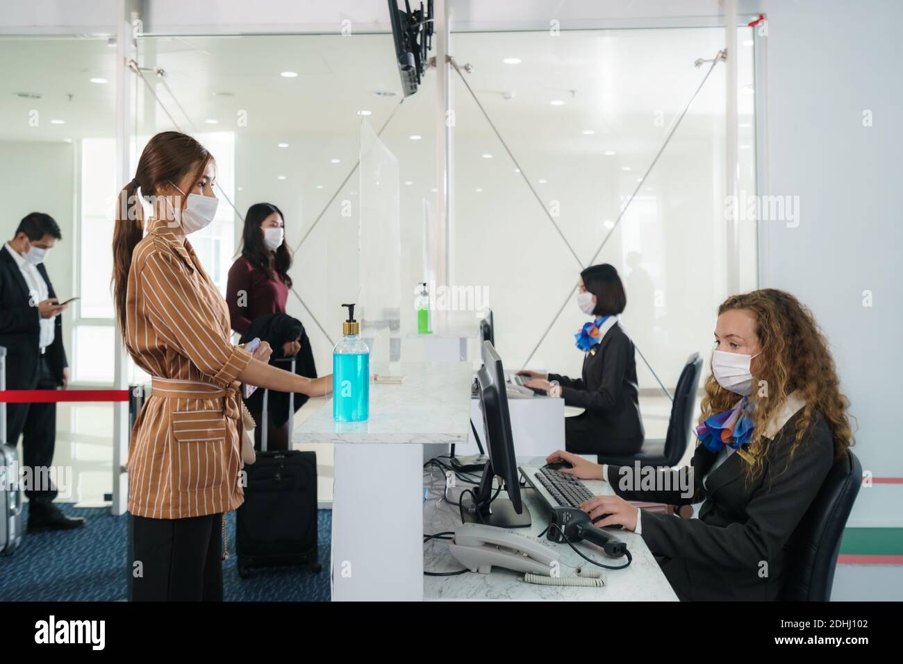 Una compagnia aerea femminile passengerwith maschera sta consegnando il suo passaporto al banco della compagnia aerea effettuare il check-in attraverso una barriera acrilica per la prevenzione delle malattie cor Foto Stock
