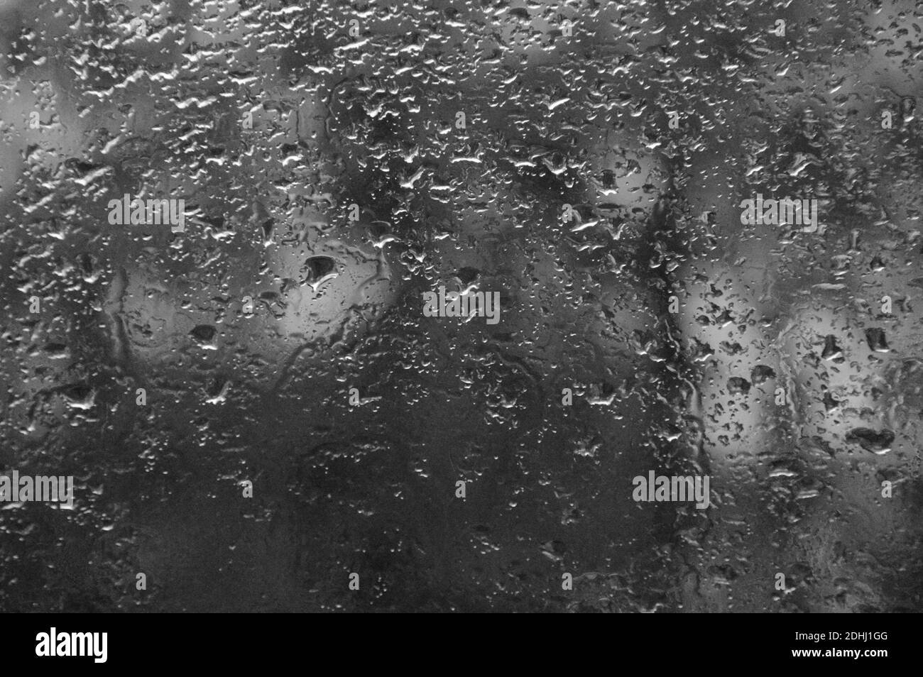Una scala di grigi di pioggia cade sulla finestra con sfondo scuro e sfocato Foto Stock