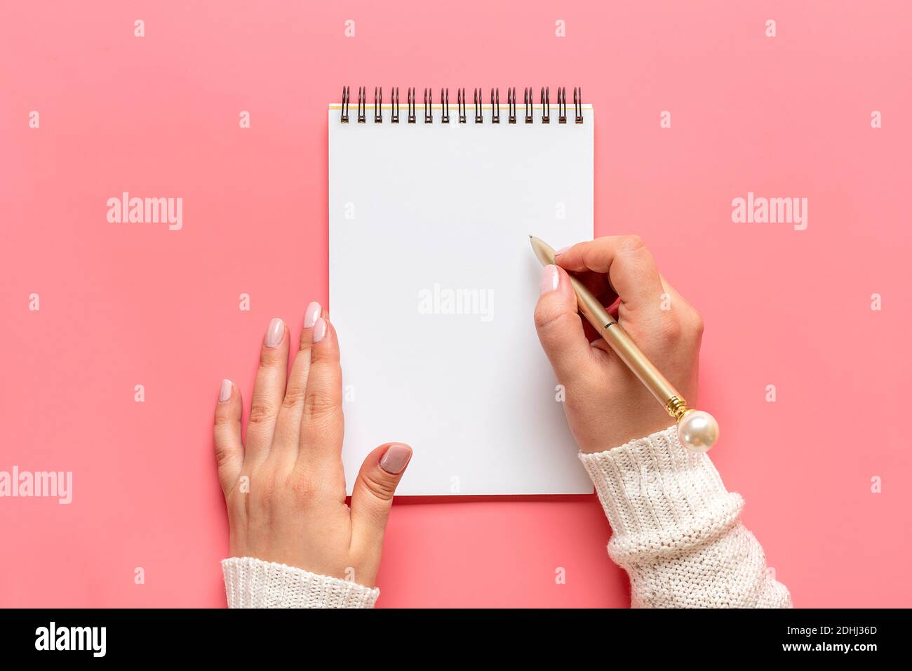 La mano femminile tiene la penna e scrive gli obiettivi di nuovo anno 2021 su notepad bianco, cactus, candela su sfondo rosa Vista superiore Flat Lay Business motivazione, idea, Foto Stock