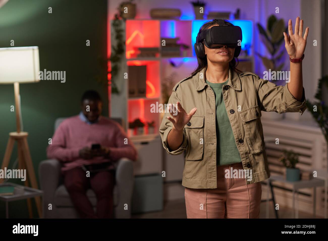 Giovane donna che indossa occhiali VR in piedi e gesturing giocando gioco di realtà virtuale Foto Stock