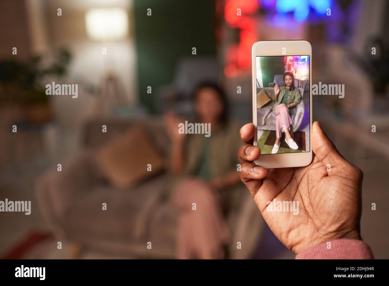 Uomo che tiene il telefono mobile fotografando la giovane donna che posa sopra il divano Foto Stock