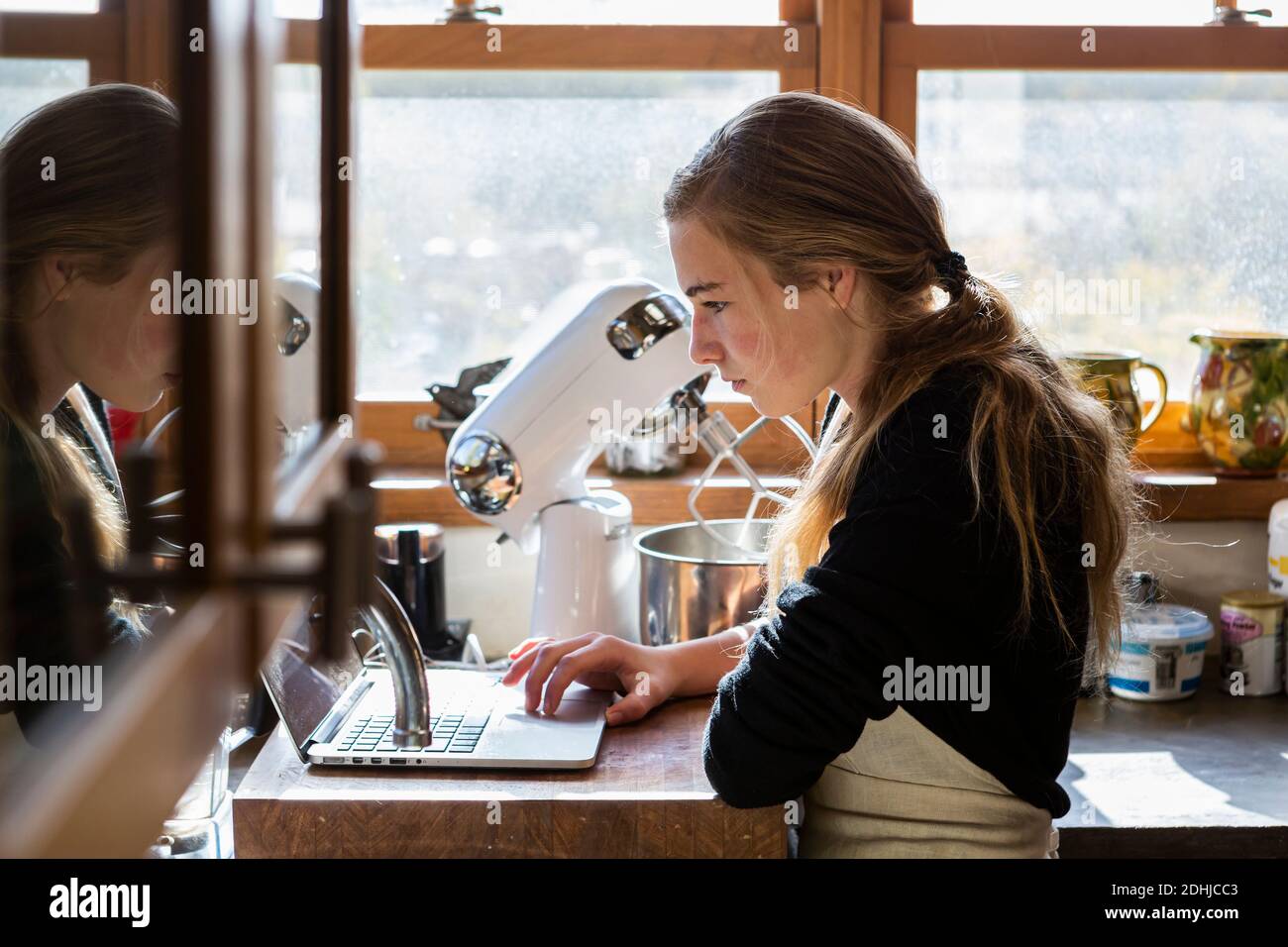Ragazza adolescente in cucina seguendo una ricetta di cottura su un computer portatile. Foto Stock
