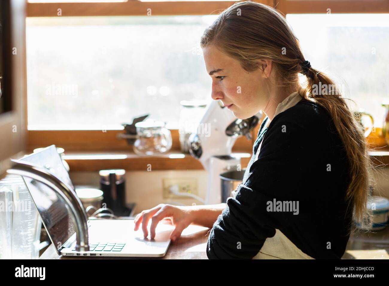 Ragazza adolescente in cucina seguendo una ricetta di cottura su un computer portatile. Foto Stock