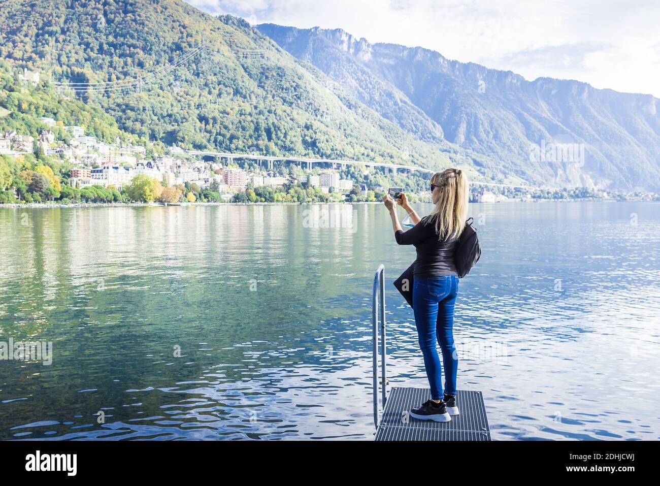 Donna che scatta una foto al Lago di Ginevra. Sta tenendo una maschera chirurgica. Concetto di nuova normalità Foto Stock