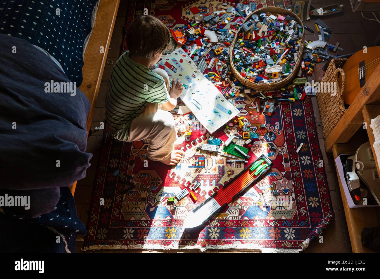 Ragazzo seduto tra i giocattoli sul pavimento della sua camera da letto in un patch di luce solare Foto Stock