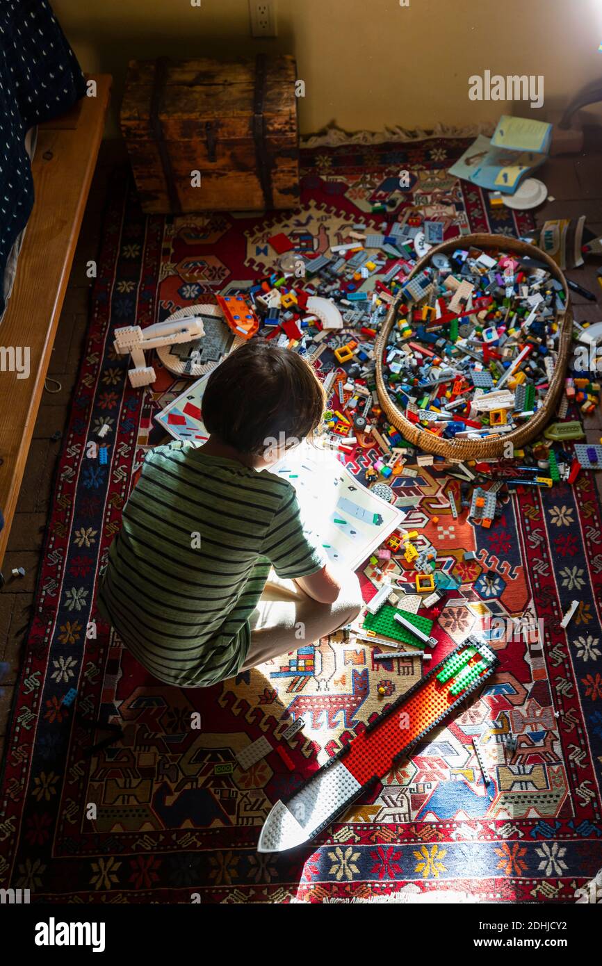 Ragazzo seduto tra i giocattoli sul pavimento della sua camera da letto in un patch di luce solare Foto Stock