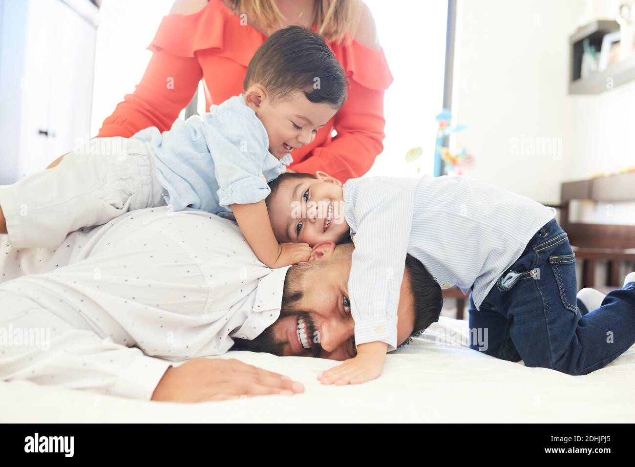 Una coppia ispanica positiva con dei piccoli figli carini che si riuniscono a letto e guardando la fotocamera mentre ti godi il passatempo a casa Foto Stock