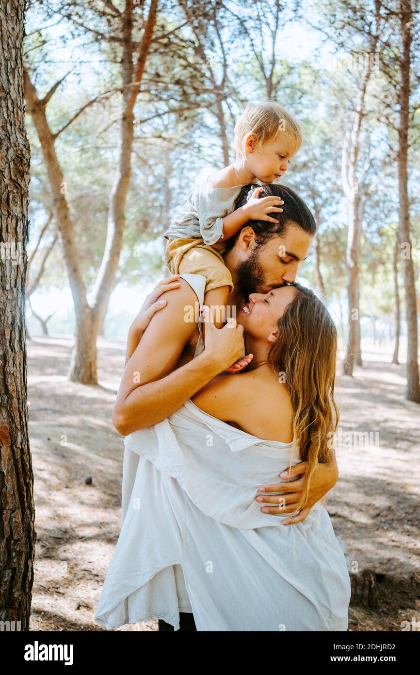 Vista laterale della famiglia multirazziale in piedi insieme in boschi e. coccolarsi teneramente mentre si passa il fine settimana in natura Foto Stock