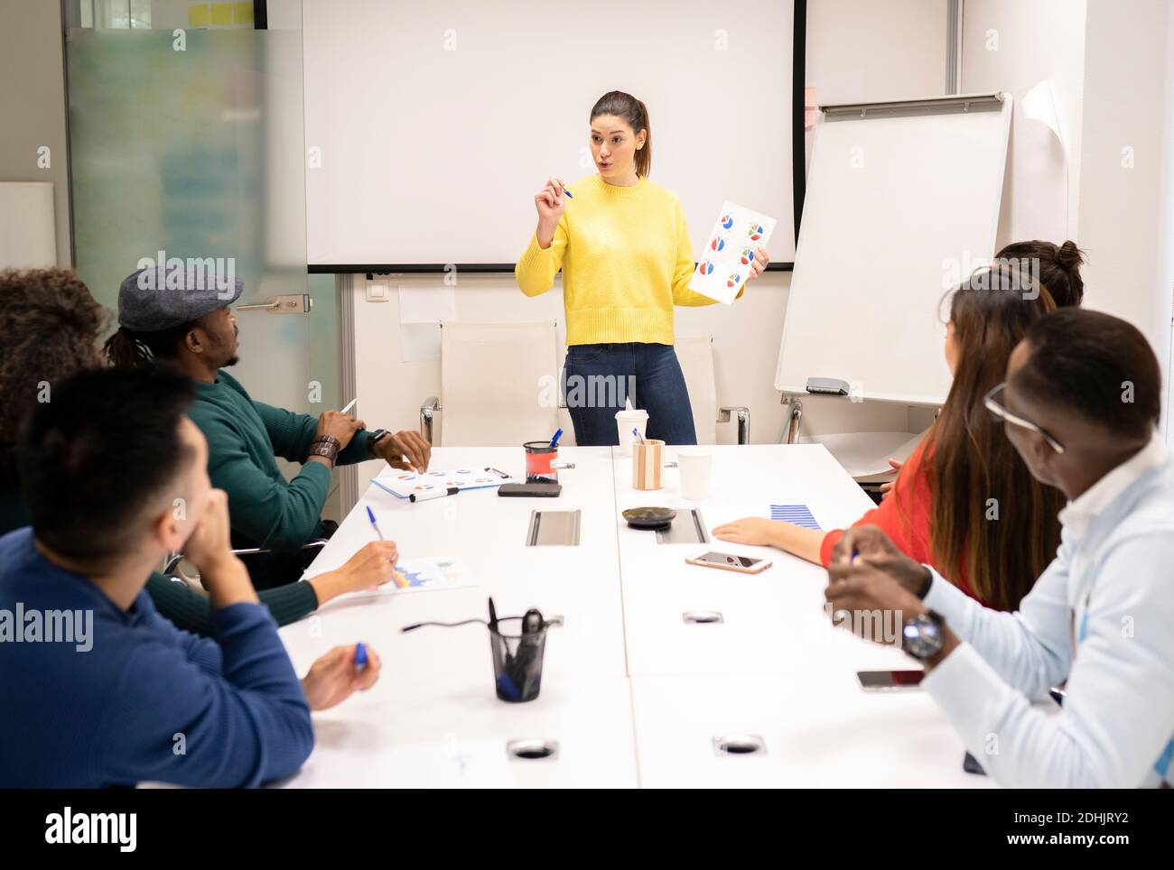 Colleghi multirazziali concentrati seduti intorno al tavolo ascoltando la voce femminile durante la presentazione e la discussione della strategia aziendale nel lavoro moderno Foto Stock