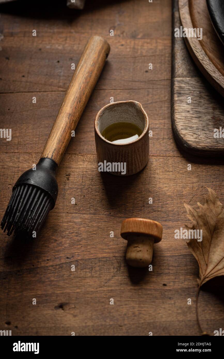 Dall'alto di spazzola per pasticceria in silicone e vasetto di olive olio disposto su tavolo di legno in cucina rustica Foto Stock