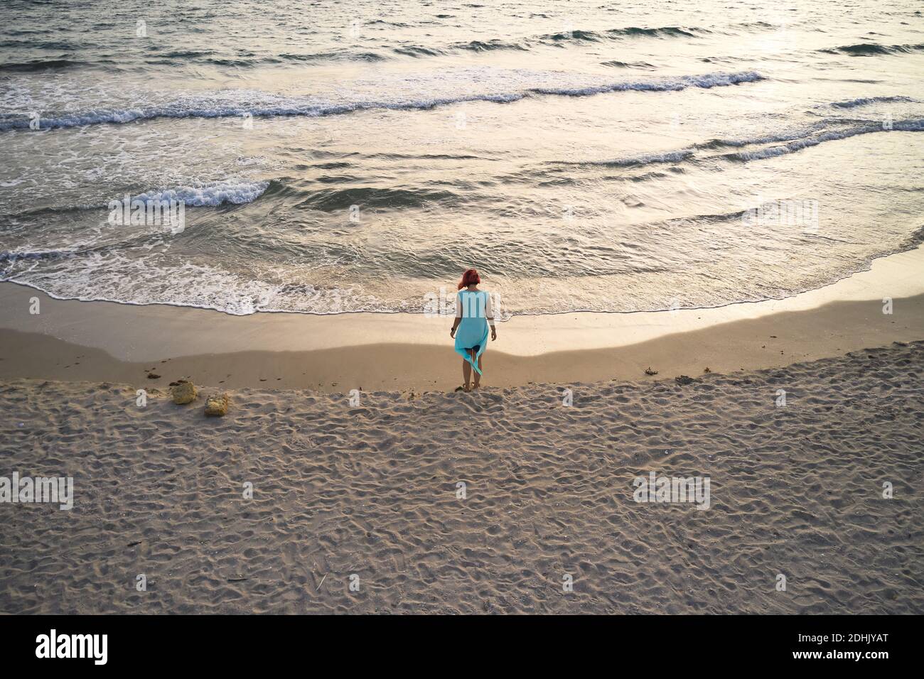 Vista posteriore del corpo di una donna irriconoscibile viaggiatore a piedi nudi su una spiaggia di sabbia vuota vicino al mare ondeggiante e godendosi fresco brezza durante l'estate h. Foto Stock