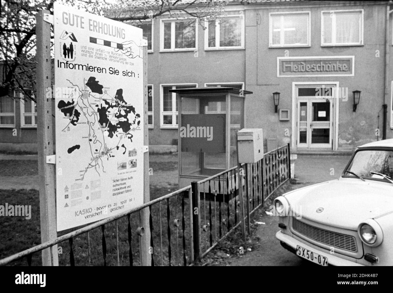 01 maggio 1982, Sassonia, Eilenburg: Un Trabant è parcheggiato di fronte al ristorante 'Heideschänke' su un parcheggio forestale con un cartello pubblicitario dell'assicurazione di Stato della RDT nel Dübener Heide nella primavera 1982. Sullo sfondo una cabina telefonica pubblica. Il cartello dice: 'Buon riposo e un viaggio di ritorno senza incidenti, la polizia stradale e la compagnia di assicurazione statale della RDT desidera che:' data esatta della registrazione non nota. Foto: Volkmar Heinz/dpa-Zentralbild/ZB Foto Stock