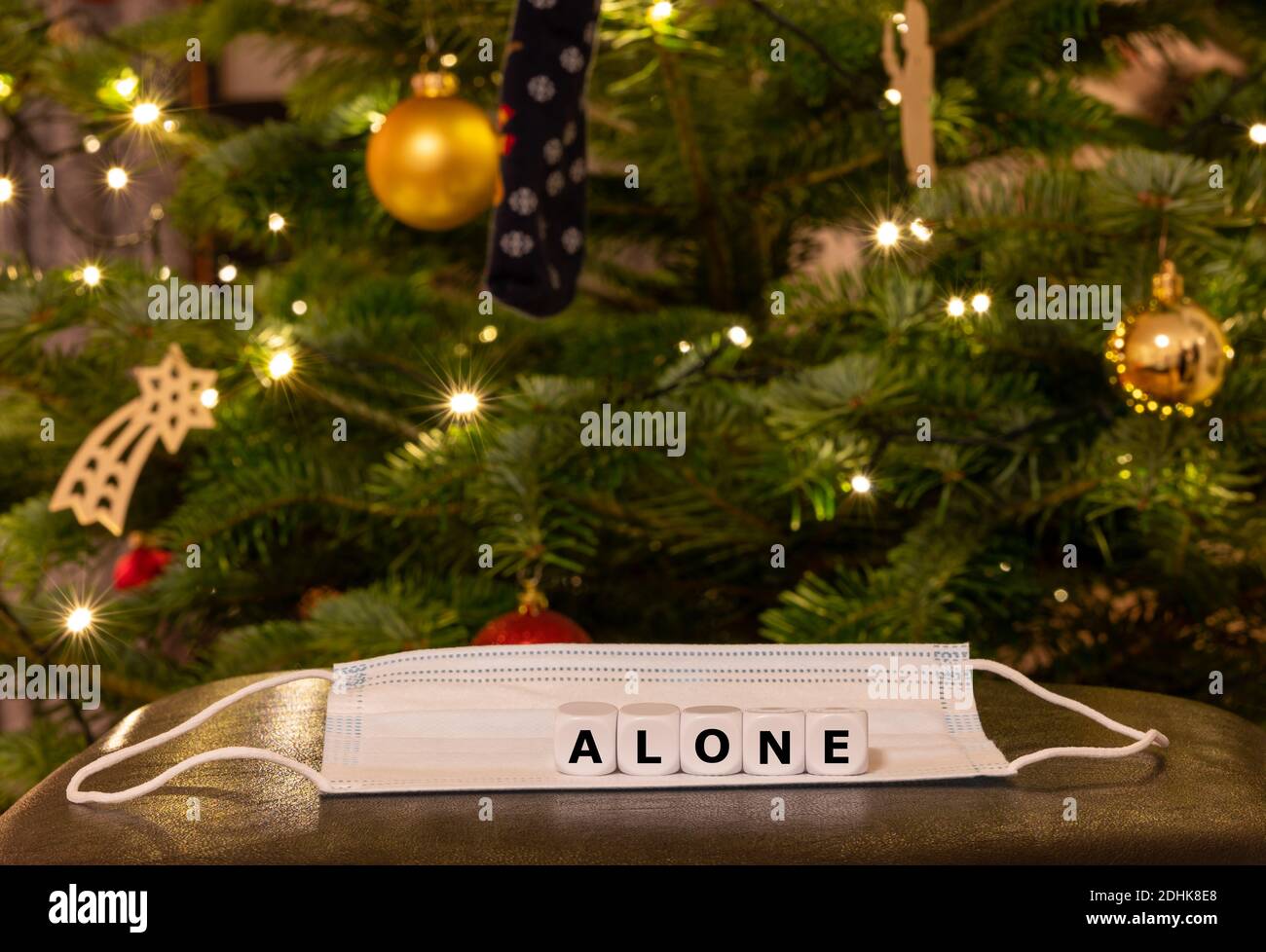 Simbolo per la gente sola durante il periodo di Natale 2020. I dadi formano la parola 'solo' sulla parte superiore di una maschera di faccia davanti ad un albero di Natale. Foto Stock