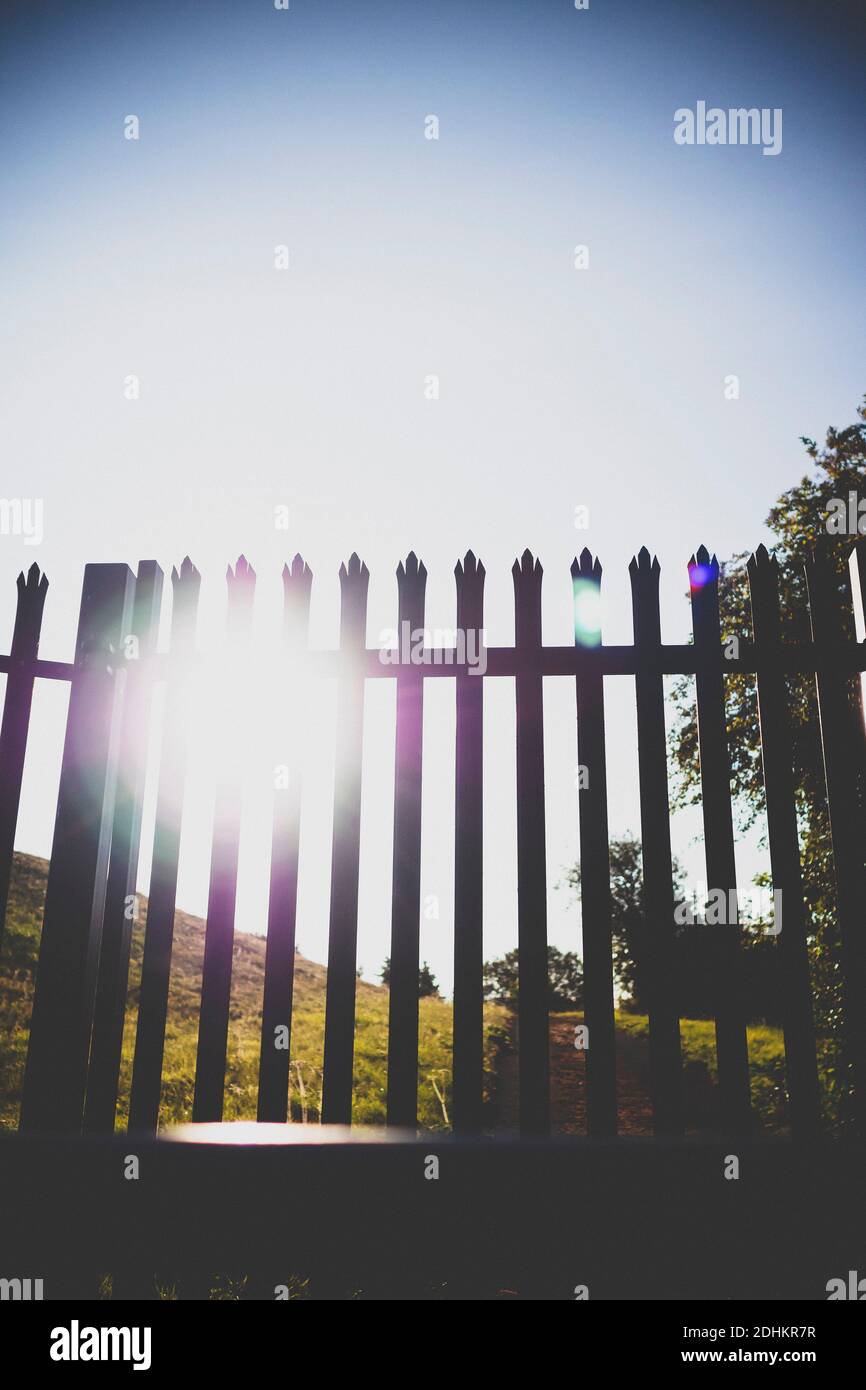 Sole basso che esplica attraverso una recinzione di sicurezza metallica che circonda una recinzione rurale. Foto Stock