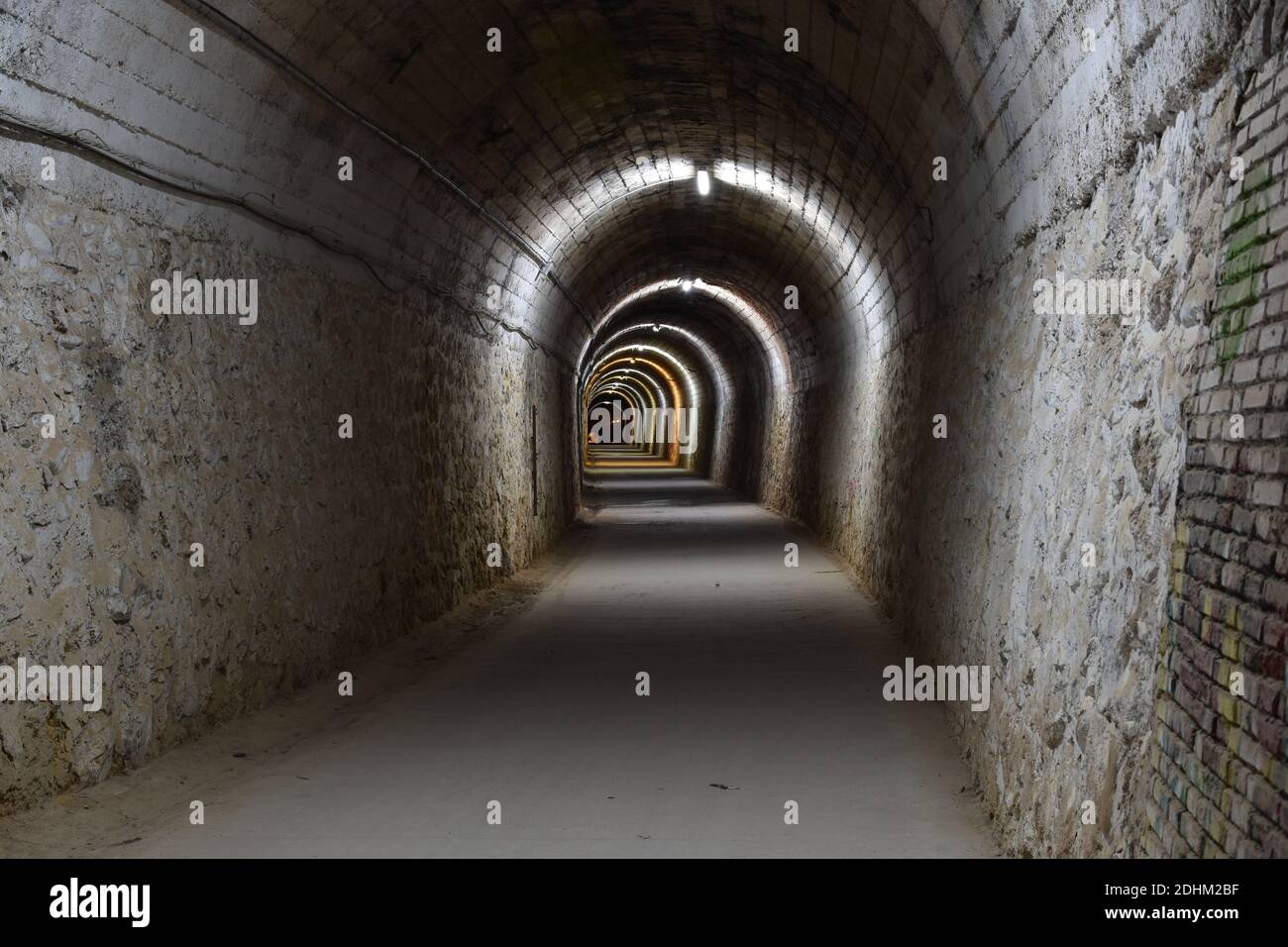 Sezione del tunnel Arnedillo costruito nella roccia, con mattoni e calcestruzzo. Luci di colori diversi e sullo sfondo l'uscita. Foto notturna. Foto Stock