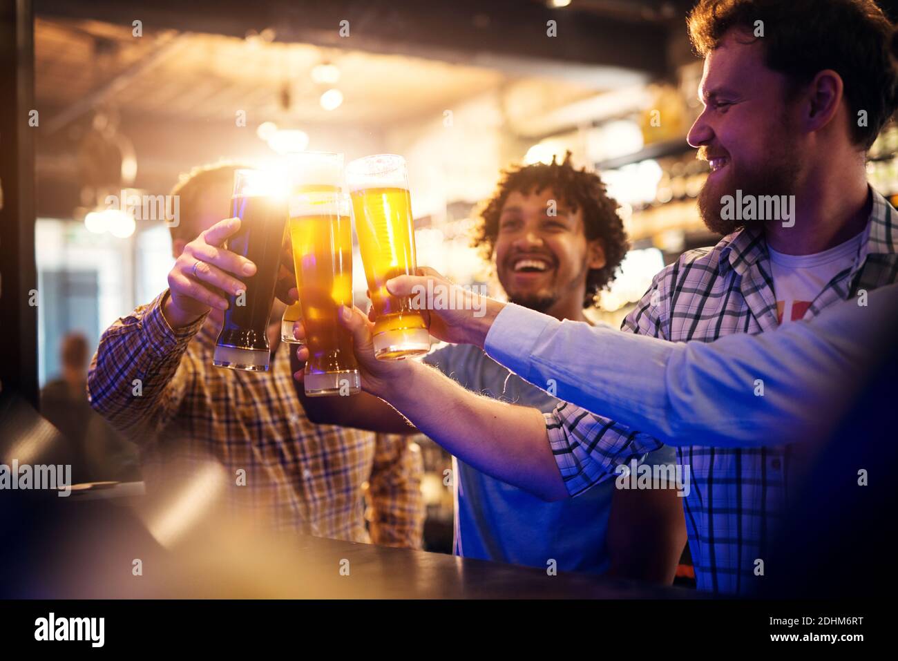 Bei amici sorridenti multiculturali che sorseggiano bicchieri di birra nel pub. Vista a fuoco di mani e bicchieri da birra. Foto Stock