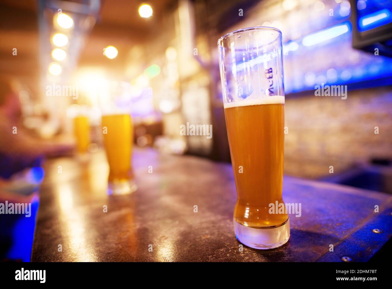 Vista ravvicinata del bicchiere di birra alla spina collocato su un tavolo da bar con una fila di altri sullo sfondo. Foto Stock