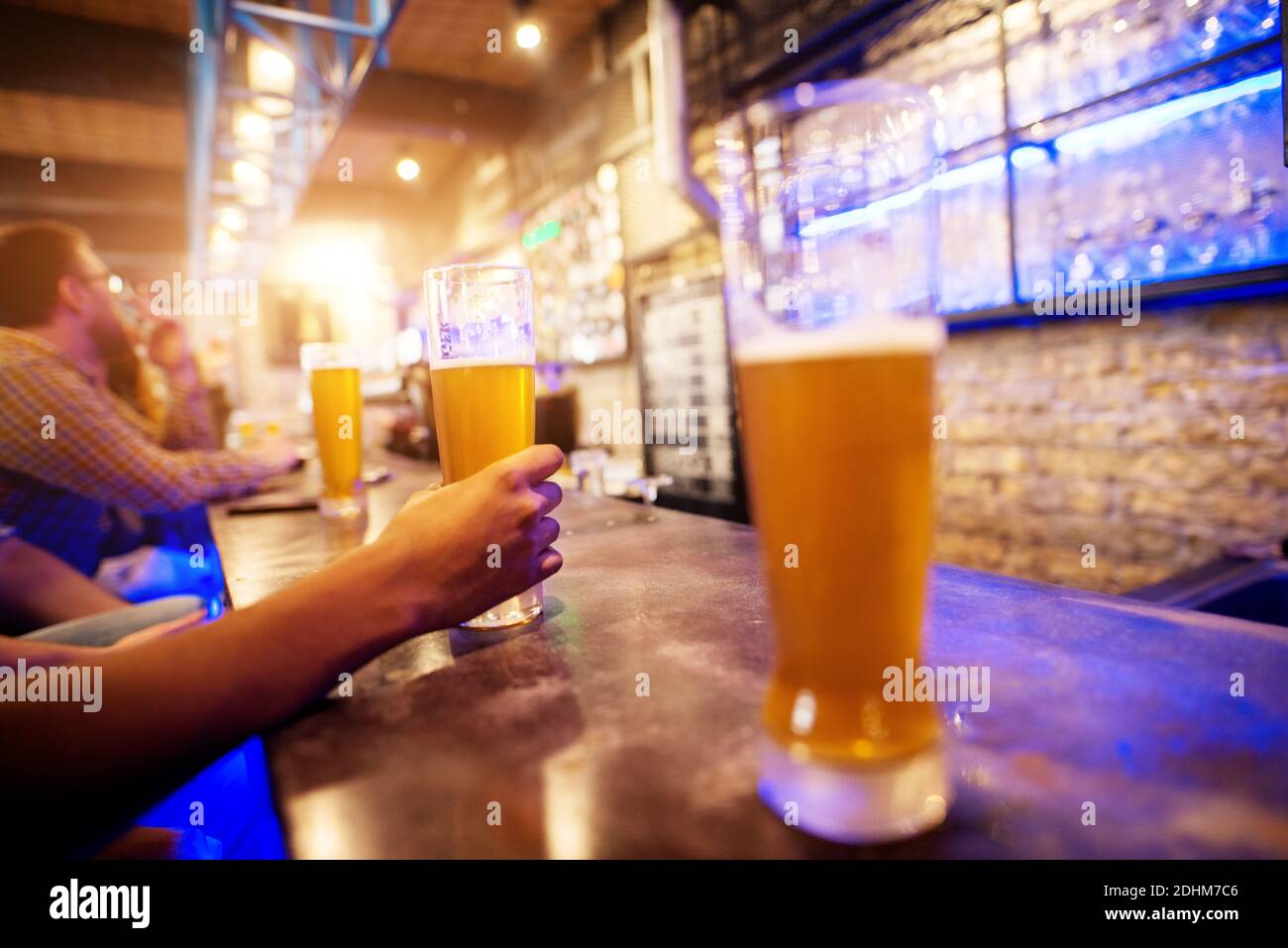 Vista ravvicinata della mano mentre si tiene il bicchiere di birra alla spina collocato su un tavolo da bar con una fila di altri sullo sfondo. Foto Stock