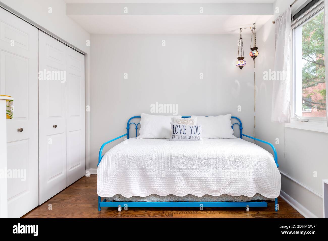 Una piccola camera da letto con un letto doppio laterale, letti blu baby corrimano, un cuscino che dice, 'Love you to the moon and back', e vetrate appese. Foto Stock