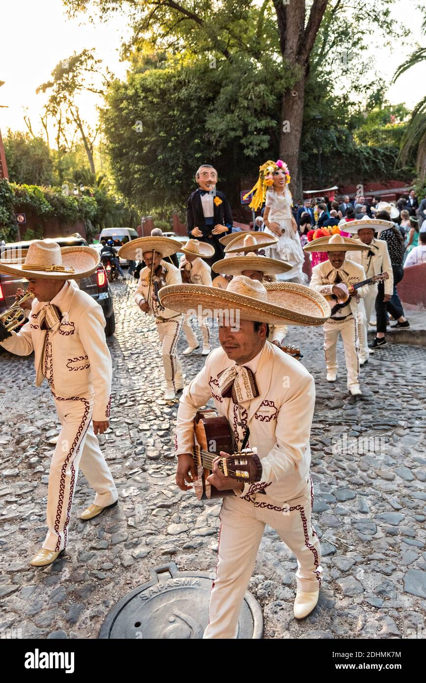 Una tradizionale banda messicana di mariachi suona come marionette giganti chiamate mojigangas danza durante una festa di nozze che pareggia attraverso le strade di San Miguel de Allende, Guanajuato, Messico. Foto Stock