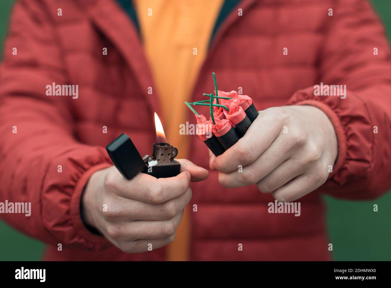 Uomo in rosso jacked illuminazione di diversi Firecrackers in mano con accendino a benzina. Guy prepararsi per il divertimento di Capodanno con fuochi d'artificio o prodotti pirotecnici Foto Stock